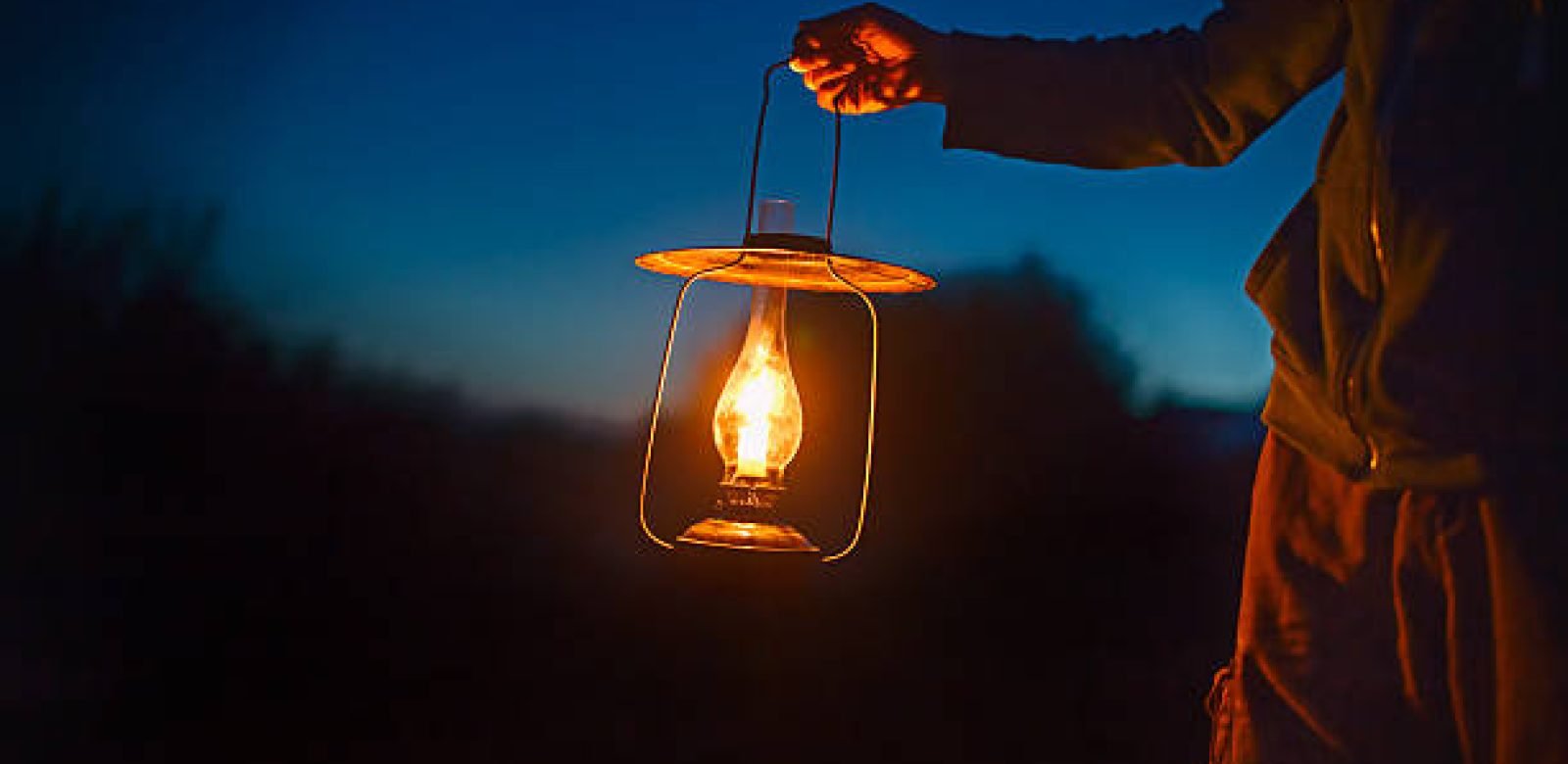 hand holds a large lamp in the dark. ancient lantern with a candle illuminates the way on a night