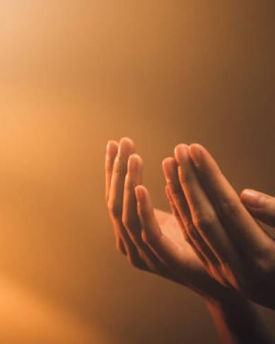 Hand praying on orange light bokeh background.