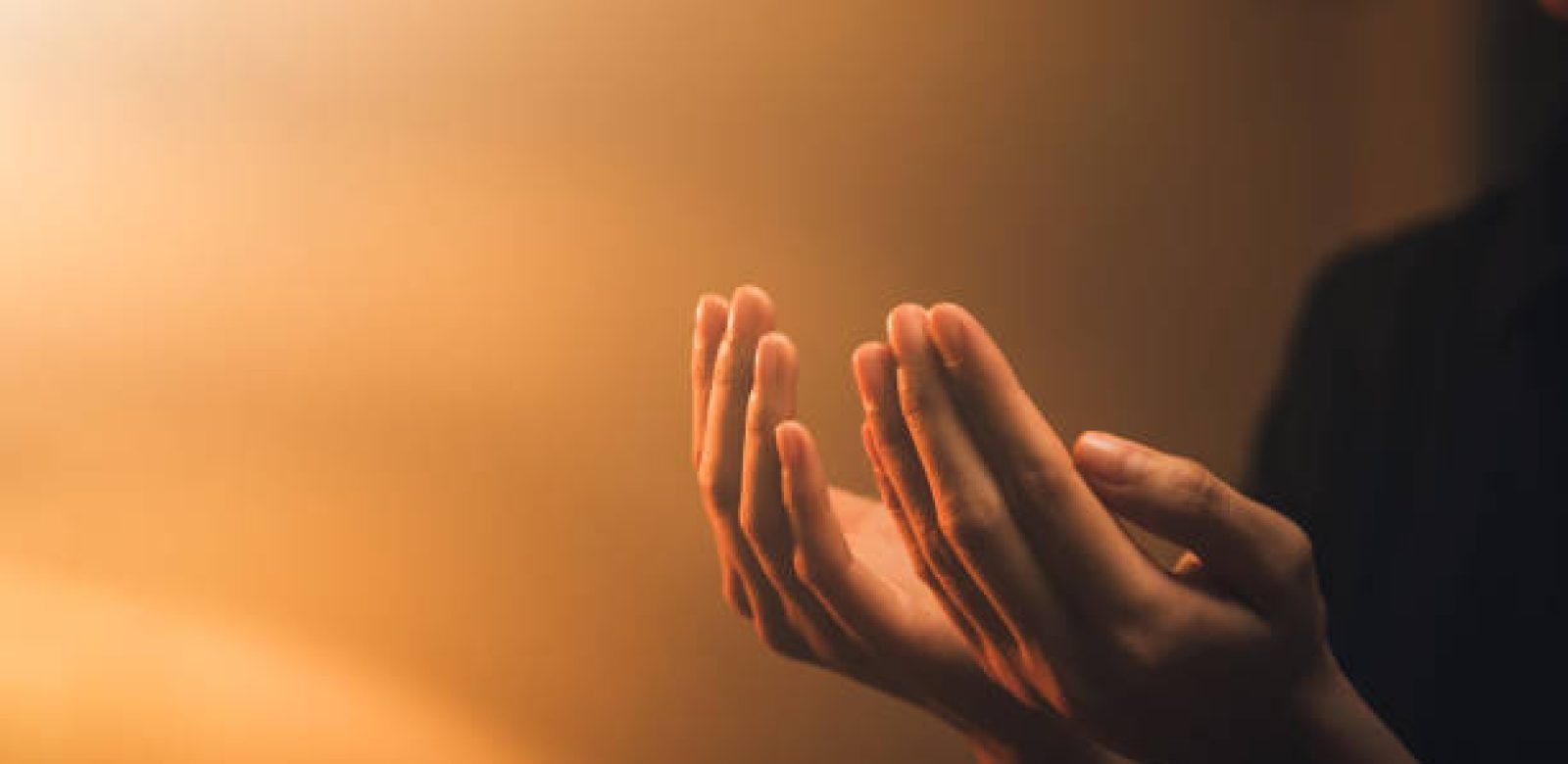 Hand praying on orange light bokeh background.