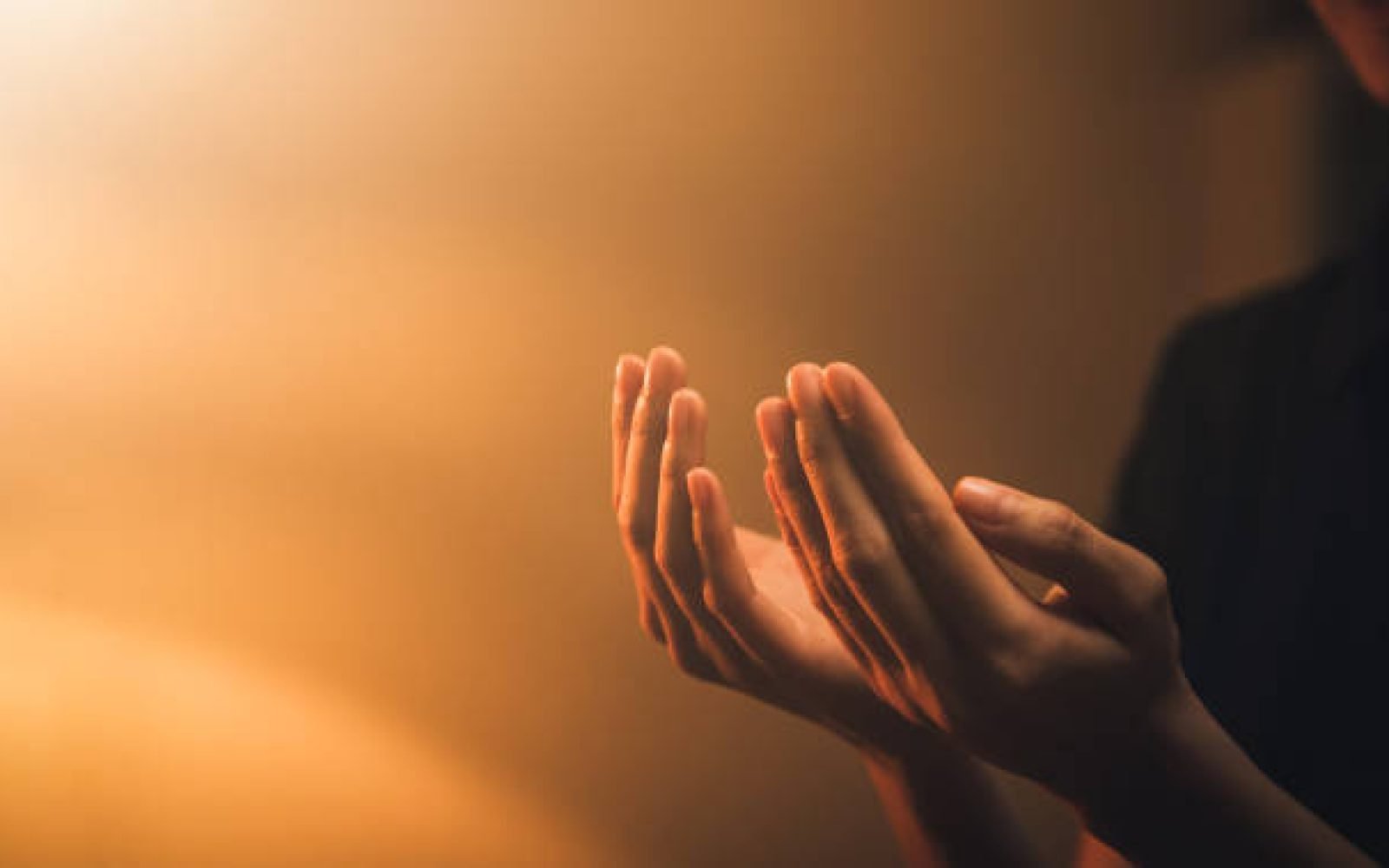Hand praying on orange light bokeh background.